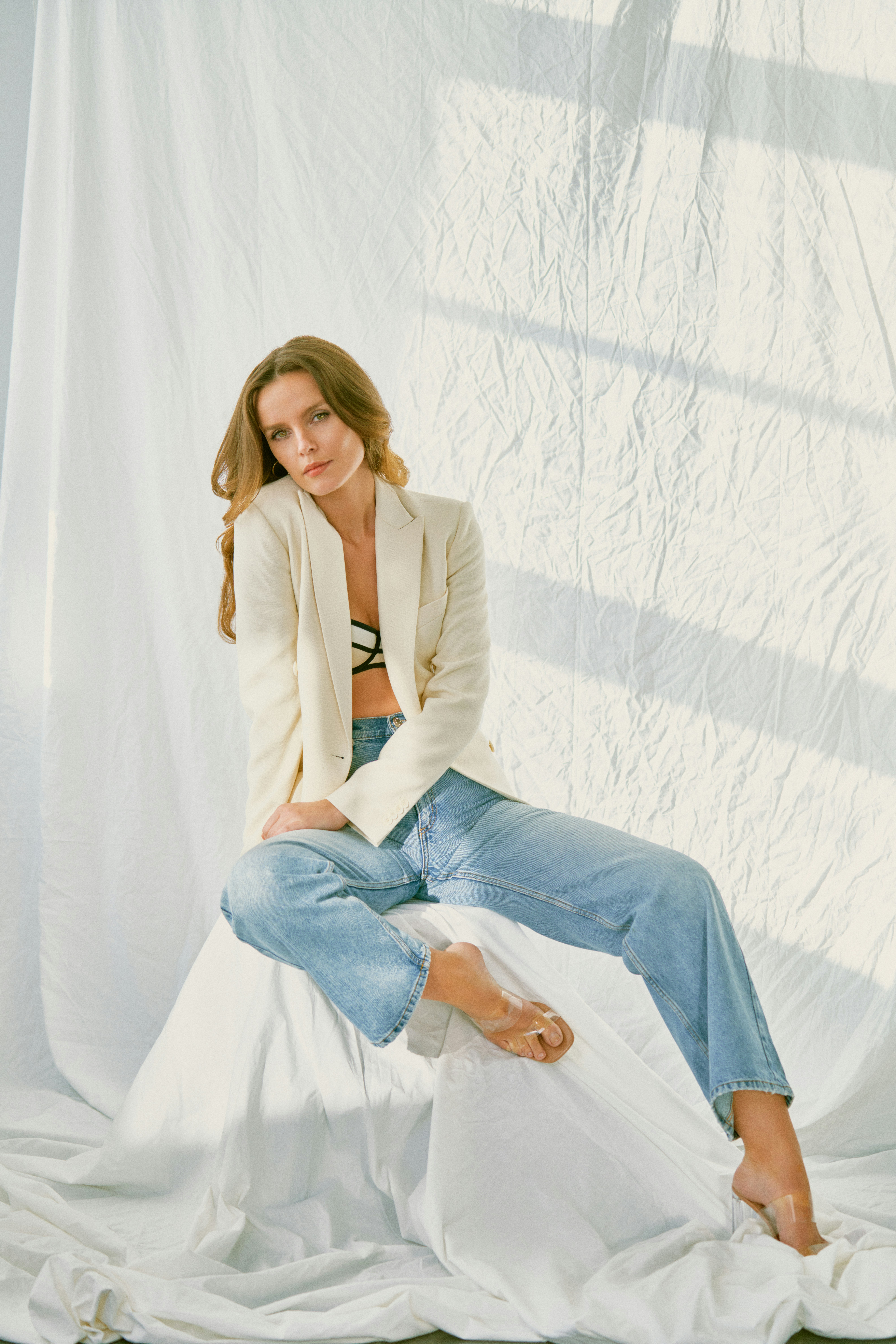 woman in brown blazer and blue denim jeans sitting on white textile